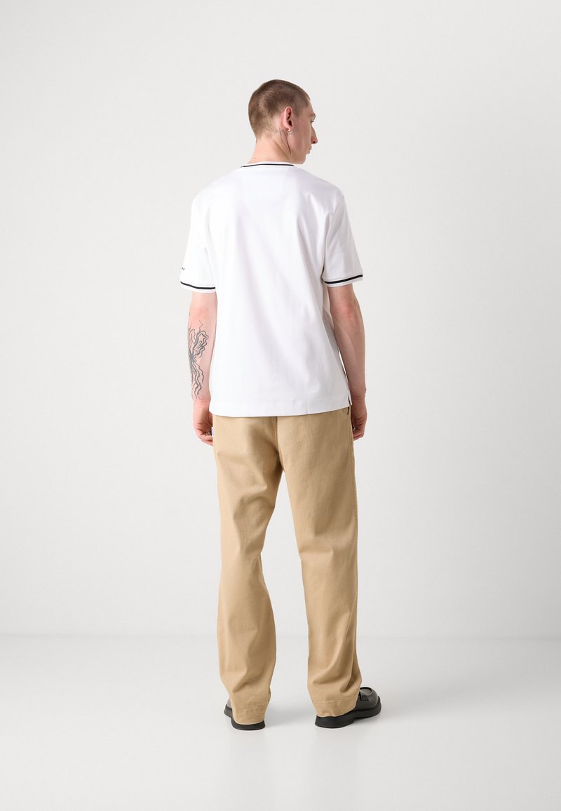 Polo bianca a maniche corte, con piping nero di accentuazione su colletto e maniche. Abbinata a pantaloni beige dalla vestibilità comoda e scarpe nere.