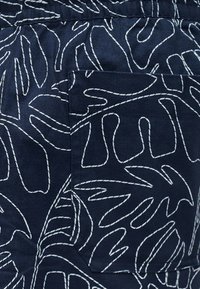 Tissu bleu marine avec des motifs de feuilles abstraites blanches cousues, comprenant une poche carrée visible au centre.