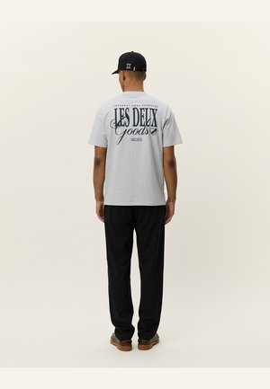 Gray cotton t-shirt with black graphic text on the back, paired with black pants and brown footwear, viewed from the back.