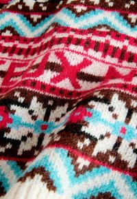 Knit sweater fabric in red, pink, blue, brown, and white. Features a geometric pattern with snowflakes and zigzag designs across the texture.