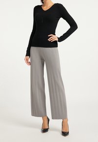 Maglione nero a maniche lunghe con scollatura a V e dettagli con bottoni, abbinato a pantaloni grigi chiari a gamba larga con righe e scarpe nere con tacco alto.