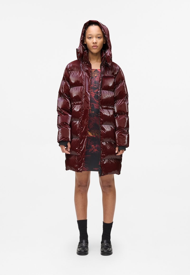 Shiny, maroon puffer coat with a hood, featuring a quilted design and front zipper. Worn over a black and red patterned dress.