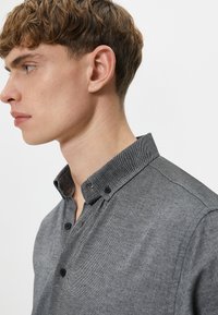 Grijze button-up shirt met een subtiele visgraatpatroon, voorzien van een gestructureerde kraag en zwarte knopen, zijaanzicht weergegeven.