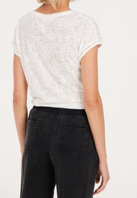 Vit, semi-transparent, texturerad t-shirt med uppvikt ärm; matchad med svarta, mjuka byxor med elastisk midja som har två bakfickor.