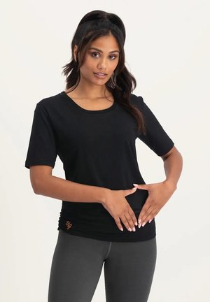 Schwarz kurzärmliges T-Shirt mit rundem Ausschnitt, weichem Material und Raffung am Saum mit einem kleinen orangefarbenen Logo.