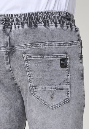 Graue Denim-Jogginghosen mit elastischem Bund und einer Gesäßtasche mit gesticktem Design und einem Etikett. Die Textur ist glatt mit einem verblassten Finish.