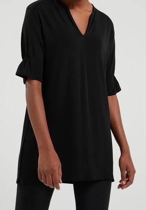 Tunic nera con scollatura a V, maniche corte elastiche e vestibilità comoda. Realizzata in tessuto morbido con fessure laterali per facilitare i movimenti.