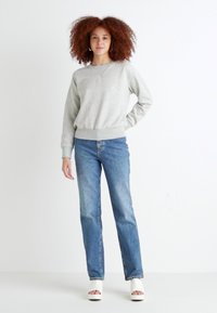 Sweat-shirt gris clair avec un ourlet côtelé, associé à un jean droit bleu moyen. Le modèle porte des chaussures blanches à bout ouvert.