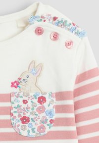 Camisa de algodón de manga larga con rayas rosas y blancas. Presenta un conejito bordado y un bolsillo floral con botones rosas y un cuello con volantes.
