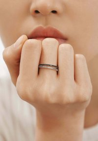 Anillos apilados en negro y plata con acentos decorativos, llevados en una mano con una apariencia natural y ligeramente texturizada.