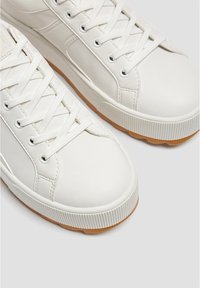 Baskets en cuir blanc avec lacets plats blancs, semelle en caoutchouc et bords texturés, présentant une finition lisse et des détails de design minimalistes.