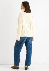Maglione spesso a treccia con colletto alto, abbinato a jeans blu larghi e zoccoli marroni con borchie lungo suola.