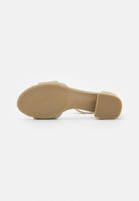 Beige High Heel Sandale mit strukturiertem Fußbett, glatter Sohle und Blockabsatz mit rutschfestem Muster.