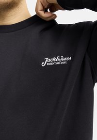 Sudadera negra de cuello redondo con un tejido texturizado. En el lado izquierdo se encuentra estampado en blanco "Jack & Jones ESSENTIALS DEPT."