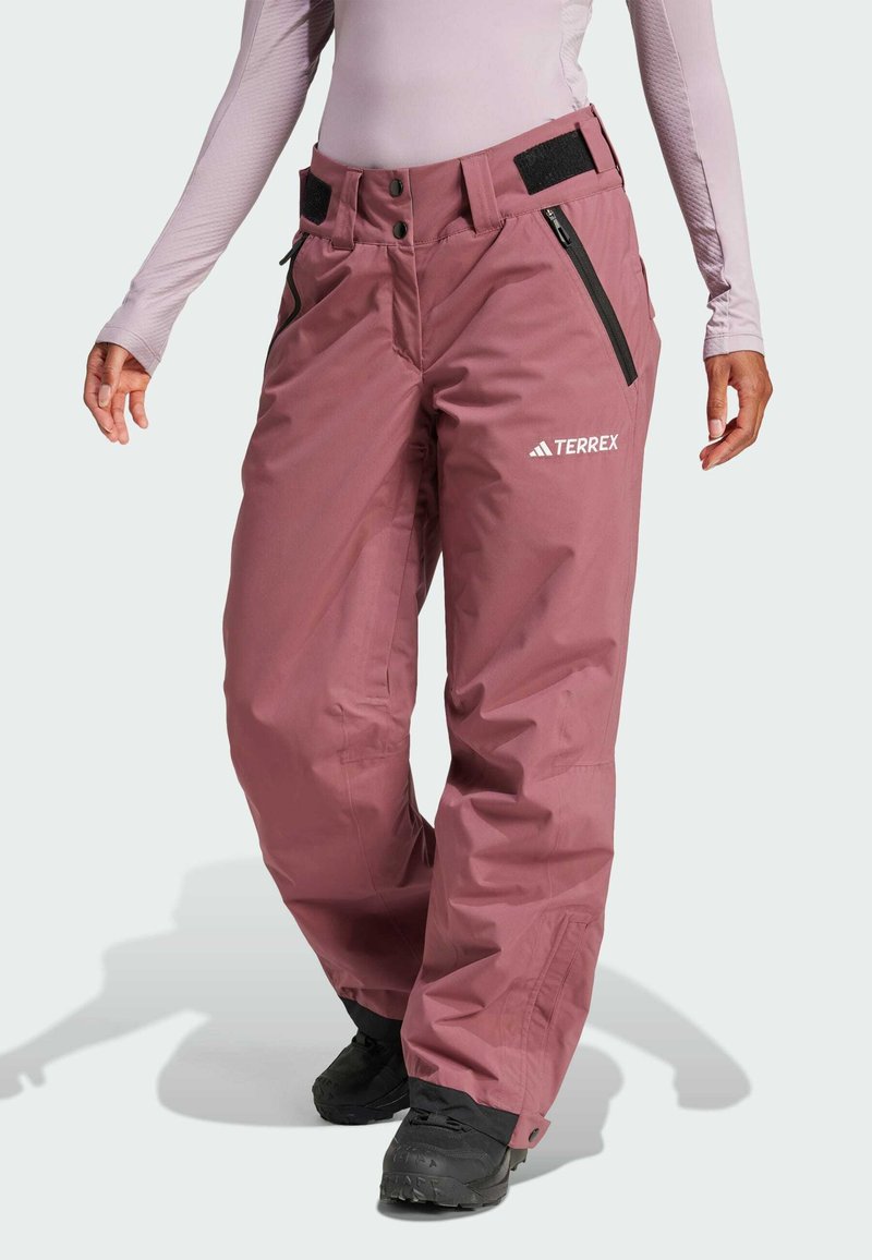 Pink waterproof snow pants with adjustable waistband, zippered pockets, and logo on the front. Fabric appears smooth and durable.
