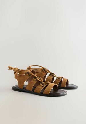 Bruine suède gladiator sandalen met open tenen, meerdere banden en een gestrikt enkel detail. Rubberzool met een gladde textuur.