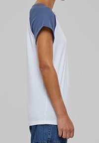 Hvid kortærmet T-shirt med blå ærmer, fremstillet af bomuld. Har en rund halsudskæring og en afslappet pasform. Let tekstur.