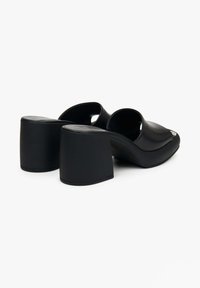 Zwarte geklede muiltjes met een glad leren buitenkant, ronde teen, open achterkant en chunky hak. Heeft een minimalistisch ontwerp zonder zichtbare hardware.