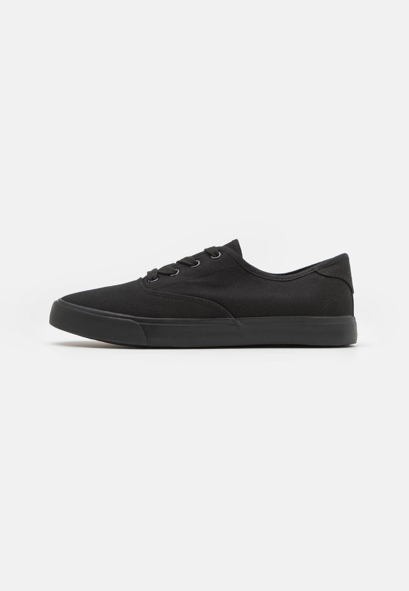 Black canvas sneakers featuring a low-top design, rounded toe, flat sole, six eyelet lacing, and textured fabric on the upper.