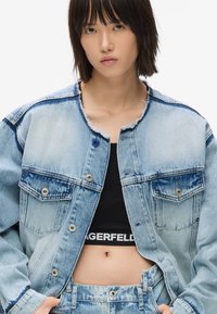 Gaiši zils džinsu jakas ar plīsušu apkakli un malām, ar divām krūšu kabatām un sudraba pogām. Saskaņota ar melnu kroptopu.