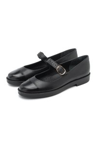 Zapatos Mary Jane de cuero negro con punta redondeada, correa ajustable y suela plana. Presentan un acabado suave y un interior con perforaciones sutiles.