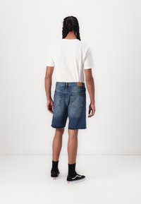 Jeanshorts med en frynset kant, lys til mørkeblå gradient, baglommer og et brunt lædermærke i taljen. Sammen med en hvid T-shirt.