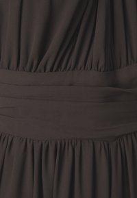 Détail d'une robe en tissu noir avec une texture plissée et une taille élastique. Matériau doux et léger avec une finition lisse et uniforme.