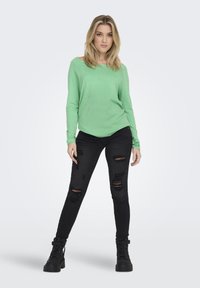Groene lange mouwen top gecombineerd met zwarte ripped jeans en zwarte veterschoenen. Soepele textuur en comfortabele pasvorm, met een casual stijl.