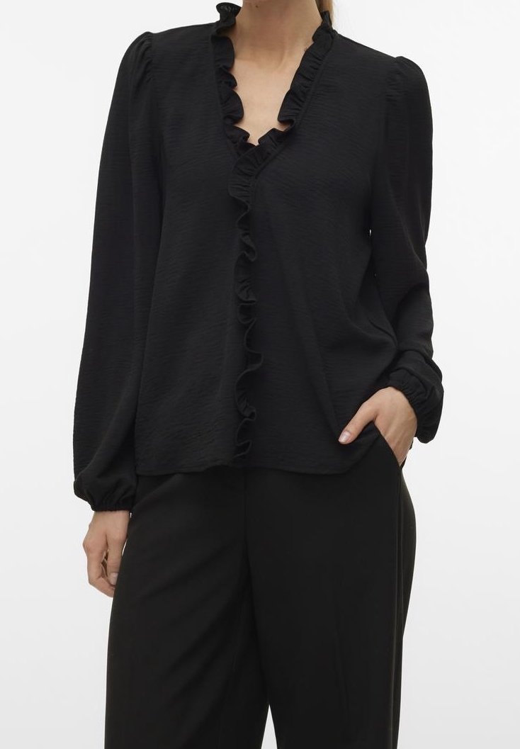 Blouse noire à manches longues et encolure en V froncée. Fabriquée dans un tissu texturé, la coupe est ample avec des poignets froncés. Associée à un pantalon noir.