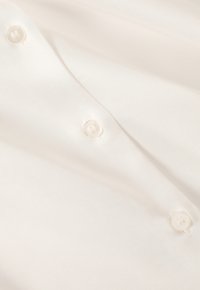 Vitt satin tyg med en slät textur och subtil lyster, med runda, genomskinliga knappar längs knäppningen.