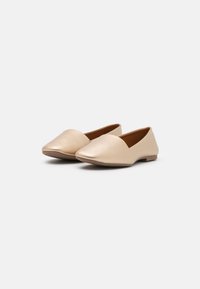 Vaaleanbeige litteät kengät, jotka on valmistettu teksturoituneesta nahasta, joissa on teräväkärkinen muotoilu ja minimalistiinen design. Kenkien pohja on litteä eikä niissä ole näkyviä metalliosia.