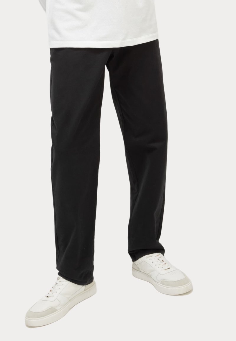 Pantaloni neri a gamba dritta in cotone, caratterizzati da una texture liscia e da una cucitura delicata, abbinati a scarpe da ginnastica bianche.