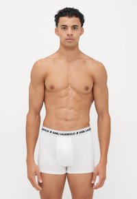 Fehér boxer alsónadrág fekete "KARL LAGERFELD" derékrésszel. Az anyag simának és struktúráltak tűnik, szorosan idomul a testhez.