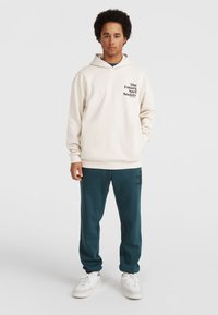 Felpa crema con logo frontale e pantaloni jogger turchesi con stampa del logo. Sneaker bianche completano l'outfit. Tessuto morbido, vestibilità rilassata.