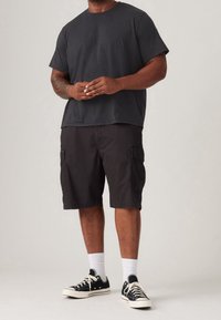 Black cotton t-shirt, loose fit, paired with black cargo shorts featuring side pockets, worn with black sneakers and white crew socks.