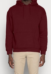 Felpa in cotone bordeaux con tasca a marsupio frontale, cordini regolabili e polsini e orlo a coste. Presenta un design a vestibilità comoda.
