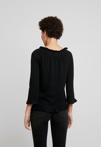 Pull en maille noire avec un col et des poignets à volants, une coupe ample, des manches trois-quarts, et un tissu texturé et doux.