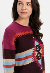 Strickpullover mit Rundhalsausschnitt, mehrfarbigen geometrischen Mustern in Lila, Blau, Orange und Braun. Strukturiertes Finish.