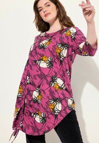 Túnica púrpura con estampado floral en blanco y naranja, con un escote redondo y mangas de tres cuartos. Detalle de cordón en el dobladillo.