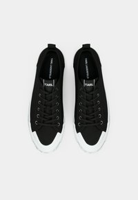 Μαύρα πάνινα παπούτσια με λευκές λαστιχένιες σόλες, με στρογγυλή μύτη, δέσιμο με κορδόνια μπροστά και λογότυπο στη γλώσσα του παπουτσιού. Απλός, λειτουργικός σχεδιασμός.