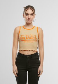 Bež crop top oranžideäärise ja "Von Dutch" logoga, tekstuurse ribikanga, lainelise äärtega, kantud kõrge vöökoha mustade teksadega.