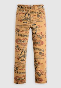 Pantalones de tela color arena con un estampado vintage de logotipos y personajes en rojo y negro, con un corte regular y diseño clásico de cinco bolsillos.