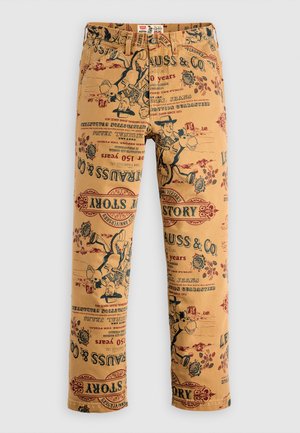 Kremové látkové kalhoty s vintage potiskem log a postav v červené a černé barvě, pravidelný střih a klasický pětikapsový design.