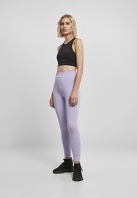 Črn crop top z širokimi naramnicami, v kombinaciji z visokim pasom in oprijetimi sivimi legicami. Črne športne čevlje dopolnjujejo obleko.