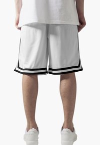 Vita nätshorts med svart kant och två horisontella ränder i fållen. Personen har på sig vita sneakers och en enkel vit t-shirt.
