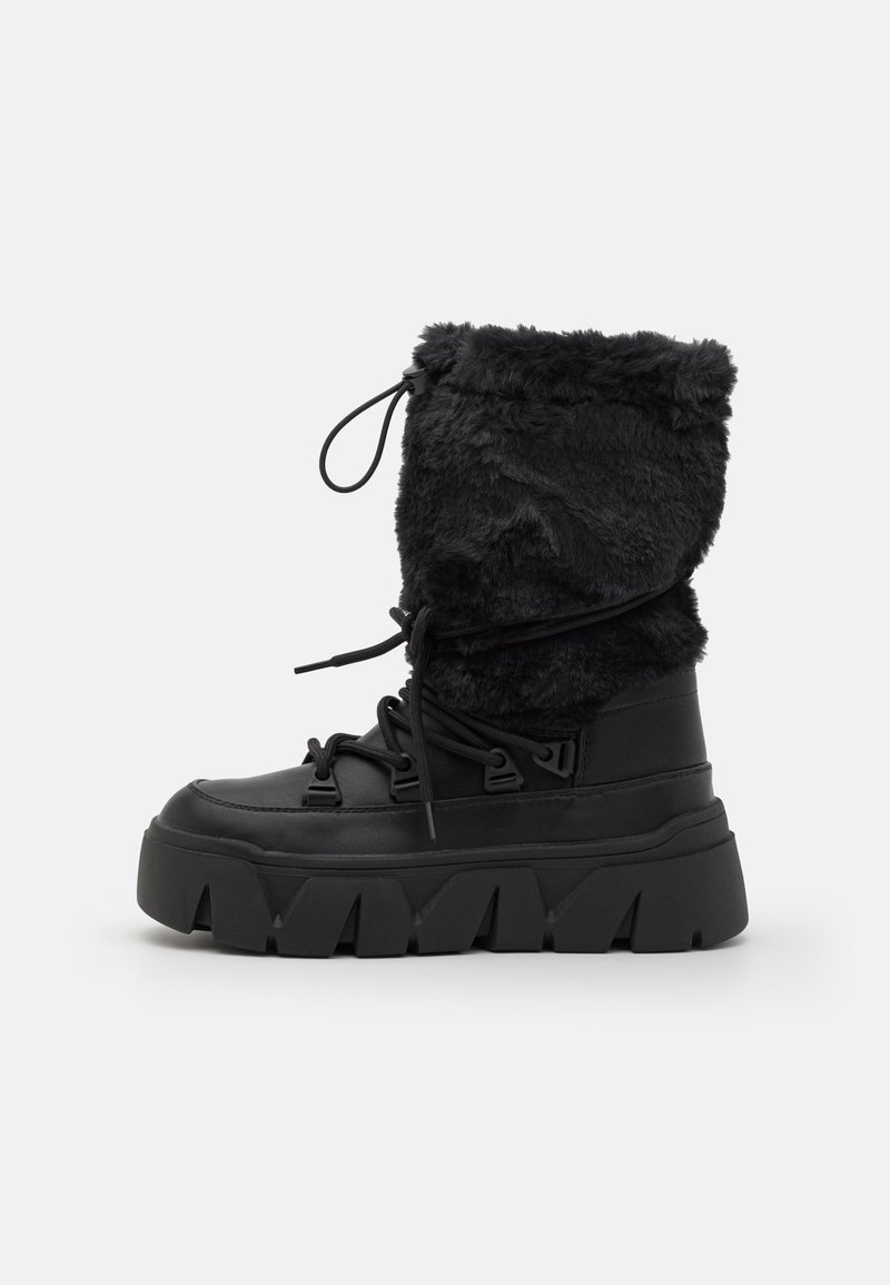 Black winter boot featuring a faux fur shaft, thick rubber sole, lacing system, and a pronounced tread pattern for grip.