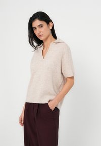 Ανοιχτό μπεζ, κοντομάνικη μπλούζα με V-λαιμόκοψη και μυτερό γιακά. Μαλακή υφή με χαλαρή εφαρμογή, συνδυασμένη με μπορντό παντελόνι.