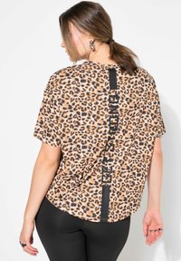 Oversized t-shirt med leopardmønster og korte ærmer, solid sort accent i midten bagpå med teksten "GET STRONG." Stoffet ser blødt ud.