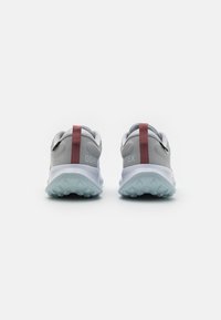 Une paire de baskets Gore-Tex grises et blanches avec des tirettes rouges, vues de l'arrière sur un fond blanc.