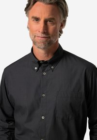 Camicia nera con bottoni, decorata con piccole pois bianchi, colletto strutturato e taschino sul petto. Realizzata in tessuto testurizzato.